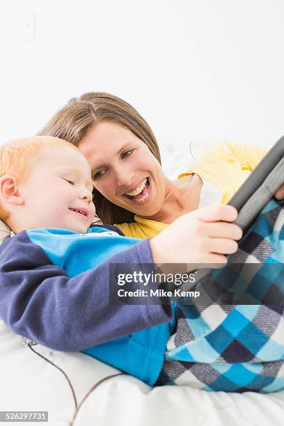 caucasian mother and son using digital tablet in bed - boy in pajamas and mom on tablet stock-fotos und bilder