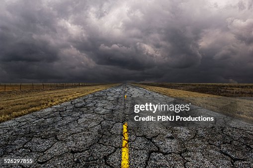 Cracked road under cloudy sky in remote landscape Cracked road under cloudy sky in remote landscape
