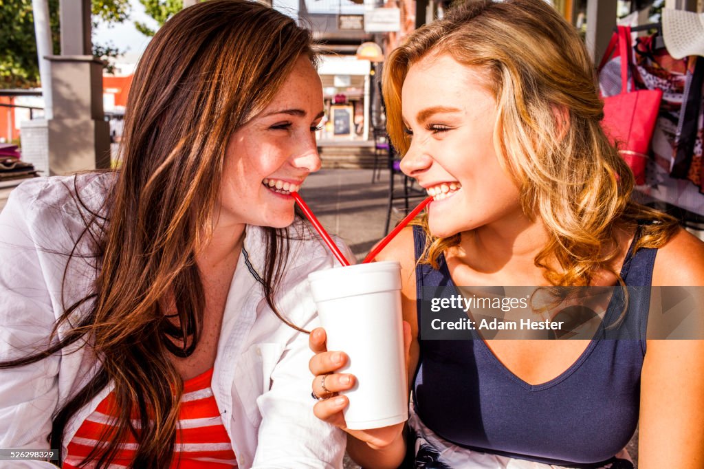 Caucasian teenage girls sharing milkshake in city