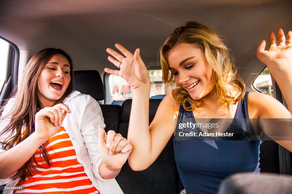 Caucasian teenage girls dancing in back seat of car