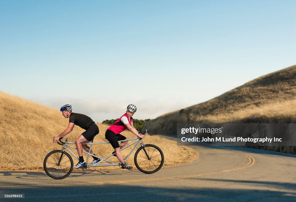 Couple riding opposing tandem bicycle on rural road