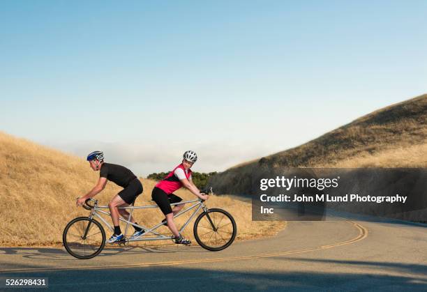 couple riding opposing tandem bicycle on rural road - tandem bicycle foto e immagini stock