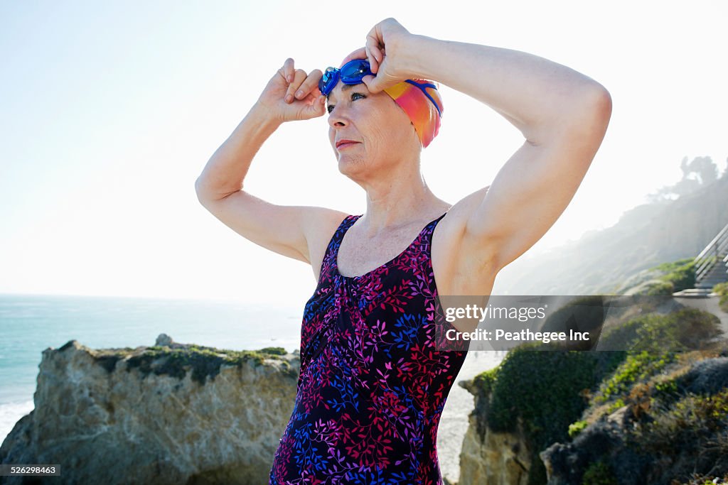 Older Caucasian woman putting on goggles on beach