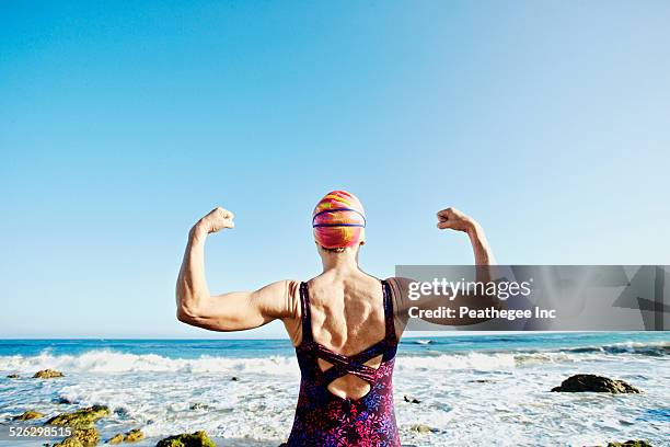 older caucasian woman flexing her muscles on beach - stiff stockfoto's en -beelden