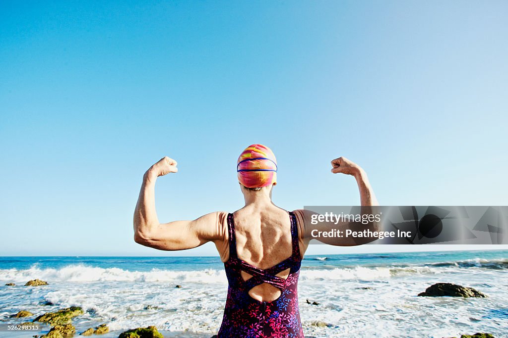 Older Caucasian woman flexing her muscles on beach