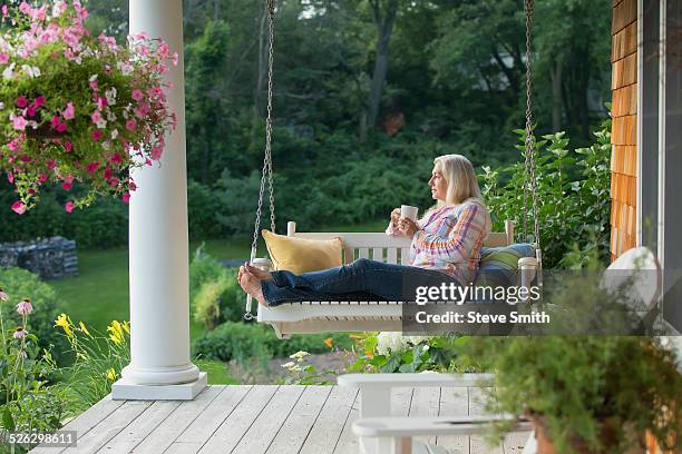 older caucasian woman drinking cup of coffee on porch swing - swing chair stock pictures, royalty-free photos & images