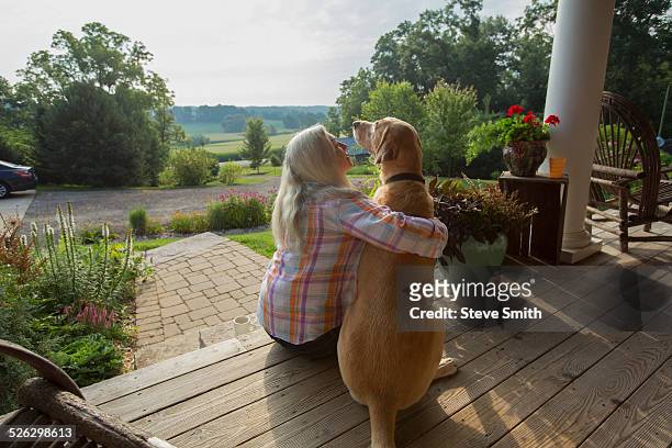 older caucasian woman petting dog on front porch - woman front and back stockfoto's en -beelden