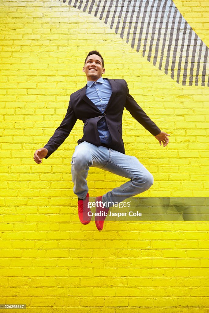 Smiling man jumping for joy near bright yellow wall