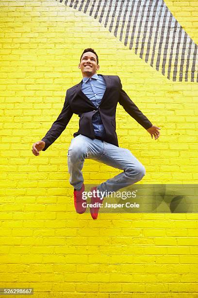 smiling man jumping for joy near bright yellow wall - stadt begeisterung stock-fotos und bilder