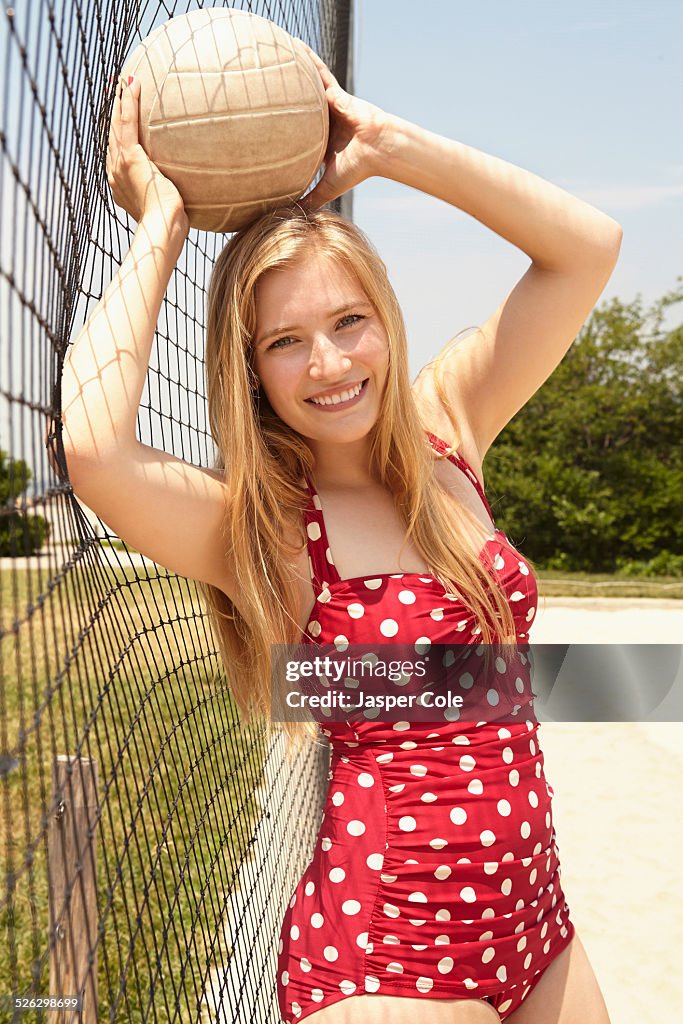Smiling woman holding volleyball near net on beach
