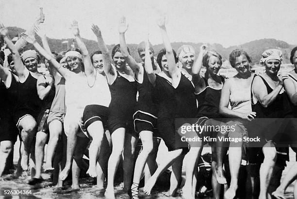 Line of young women show some leg and wave their arms as they party on the beach during the Roaring 20s.