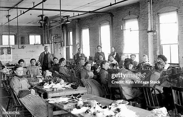 Working women behind sewing machines pause to have a photograph made of them in a garment factory early in the 20th century.