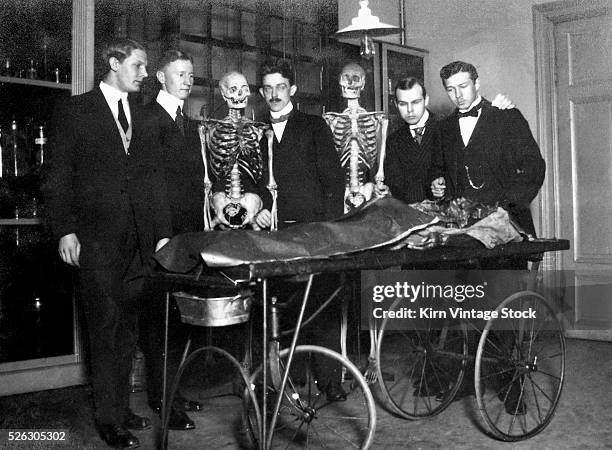 Medical students and some "skeletal" friends survey a cadaver on a gurney at a hospital in Sweden in the early 20th century.