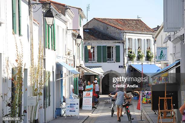 Tourists riding bikes and having a walk, "rue du Marche" street at La Flotte-en-Re. Tourist destination, Isle of Rhe , summer 2011.