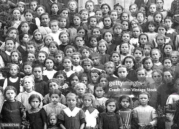 Large group of girls pose with a farm harvest on the steps of a school or orphanage.