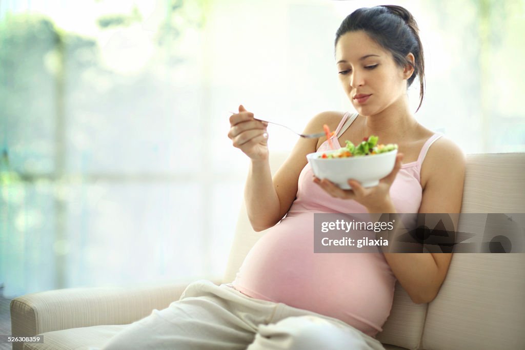Pregnant woman relaxing at home and eating salad.