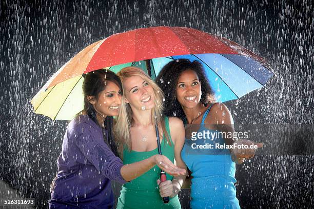 three multi-ethnic young women with umbrella enjoying rain - white and black women and umbrella stockfoto's en -beelden