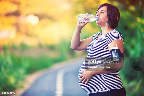 pregnant woman drinking during exercise - fitness armband stockfoto's en -beelden