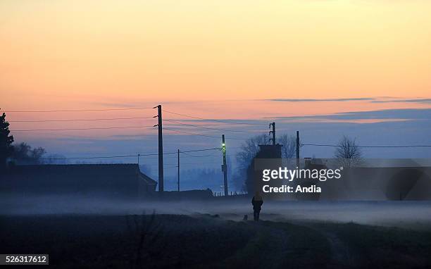 Man walking alone in the mist in the evening, in a rural village. Rural village of Sameon in Scarpe-Escaut Regional Nature Park: silhouette of a man...