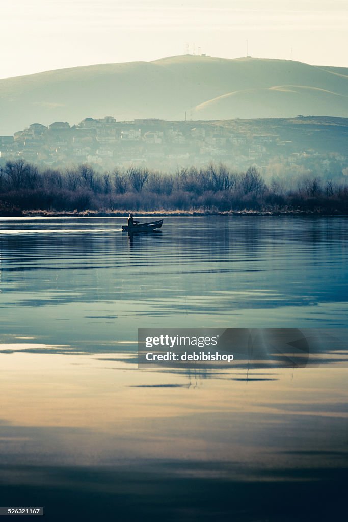 Fisherman in canoe gliding across tranquil water