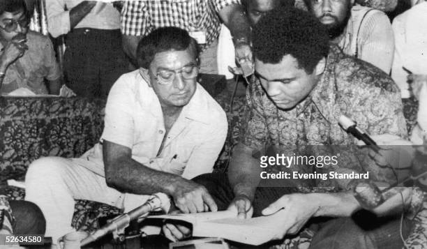 Heavyweight boxing champion Muhammad Ali looks at a book with his manager Angelo Dundee, 25th June 1975.
