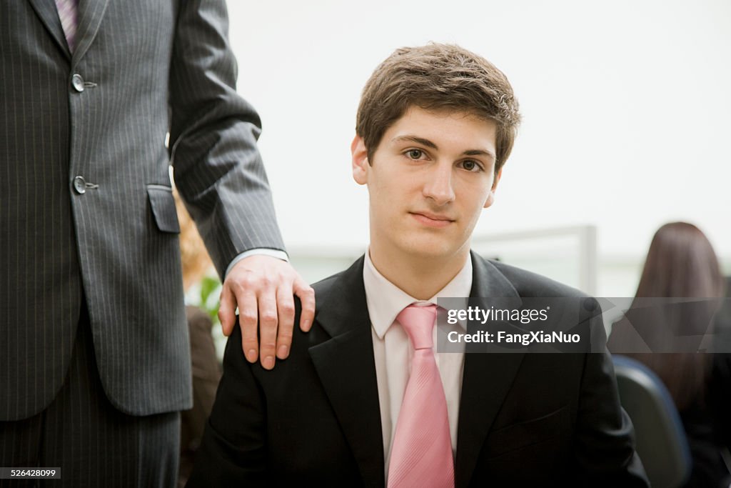 Mann sitzt im Büro mit Chef hinter ihm