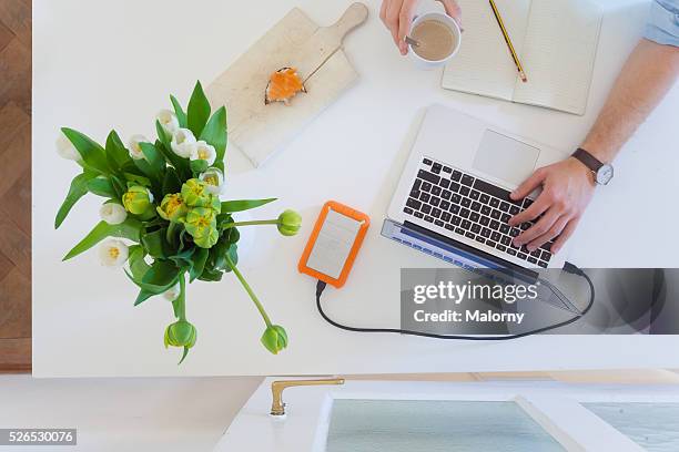 man working at home office with laptop while drinking coffee - flower arm fotografías e imágenes de stock