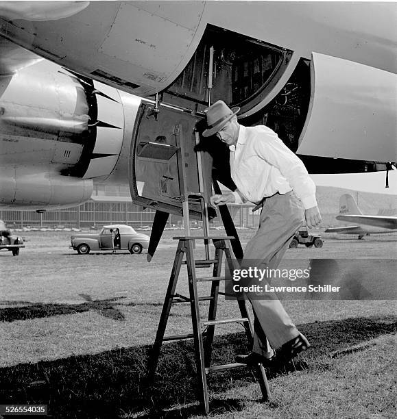 View of American businessman and aviator Howard Hughes on a stepladder beneath one of his airplanes, Los Angeles, California, 1947.