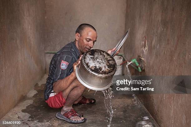 Migrant construction worker cleans cooking pots in an open air wash-room at a workers' camp in al-Khor, Qatar, on June 17, 2011. According to the...