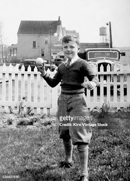 Young boy tosses a baseball in his backyard, ca. 1936.