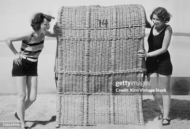 Two young women eye each other around a beach chair in Germany.