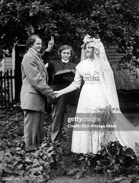 Two women, one dressed as a man, appear to be being married by a woman clergyperson.