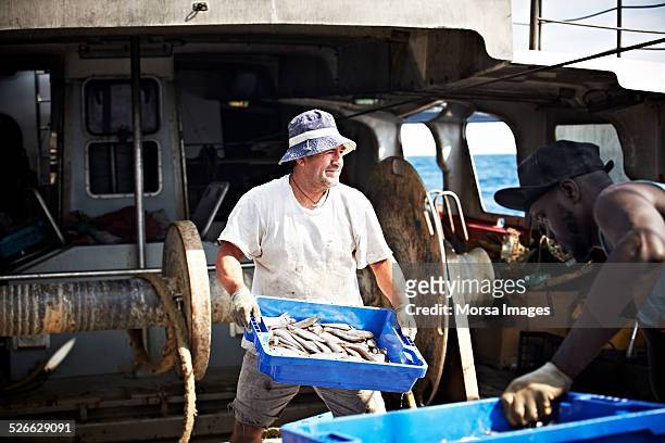 worker carrying fish crate on trawler - pêcheur photos et images de collection