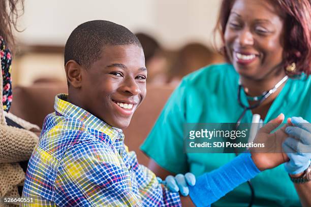 preteen boy smiling while having injured arm examined by nurse - african injured stock pictures, royalty-free photos & images