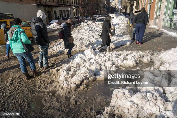 Pedestrians slog through puddles of slush and snow during their morning commute at street crossings with snow dam clogged storm drains in the Chelsea...