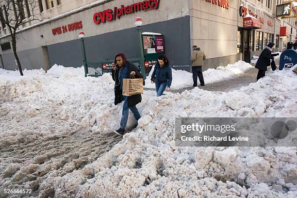 Pedestrians slog through puddles of slush and snow during their morning commute at street crossings with snow dam clogged storm drains in the Chelsea...