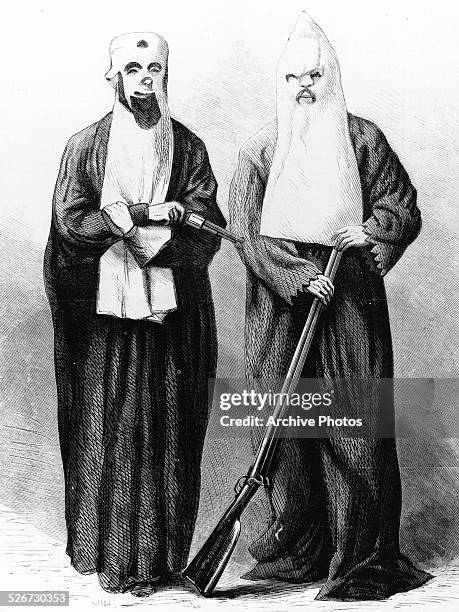 Engraved illustration depicting two members of the Klu Klux Klan, wearing hoods and holding weapons, circa 1860.