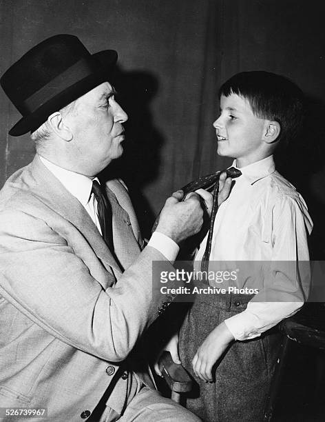 Actor Maurice Chevalier helping young Martin Stevens with his tie, on the set of the movie 'Count Your Blessings', circa 1958.
