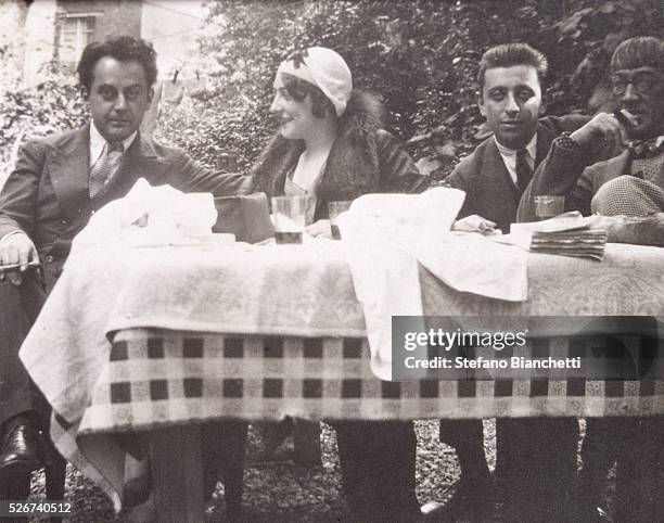 American artist Man Ray, Madame Auspach, French poet Robert Desnos, and French artist Tsugouharu Foujita sit at a table outdoors. | Located in:...