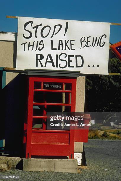 Sign above a telephone booth in the Te Anau area protests the proposed raising of Lake Manapouri. The proposed dam will provide hydroelectric power...