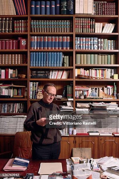 Portrait of the composer Ennio Morricone as he stands by a bookcase. Rome, Italy.