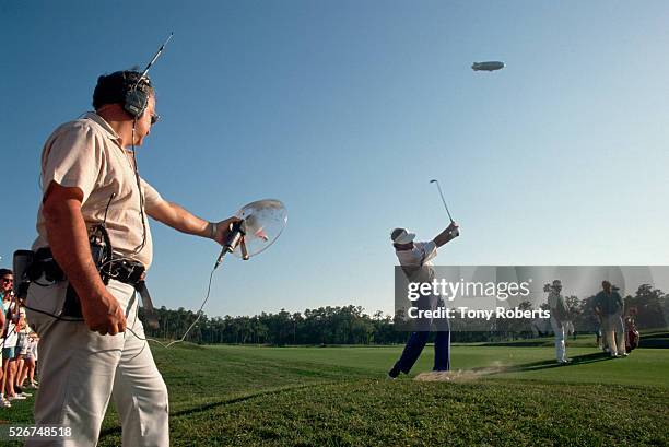 Sound engineer Gino Guarna holds a microphone out to capture the sound of a slice made by PGA member Jim Gallager as he sends a ball down the fairway.