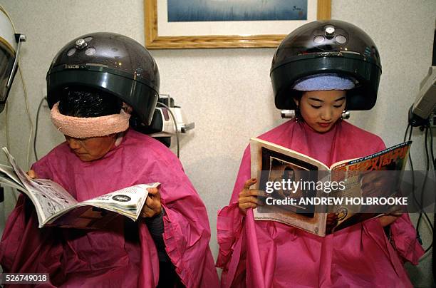 Women at a beauty salon having their hair done read magazines; one of which has Arnold Schwarzenegger on it's cover.