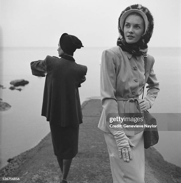 Two women model winter suits by Hattie Carnegie with Sally Victor hats along the Massachusetts coastline.