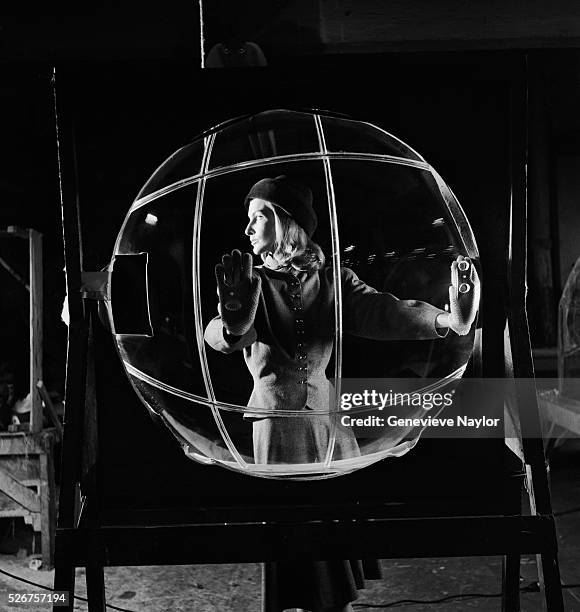 Model stands in a B-52 bomber plastic bubble. She is dressed in a Hattie Carnegie wool dress.