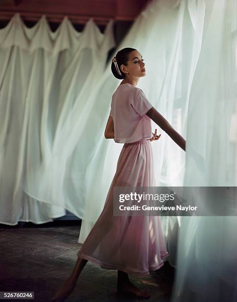 Fashion model poses in a nightdress and bolero jacket designed by Odette Barsa near some sheer drapes.