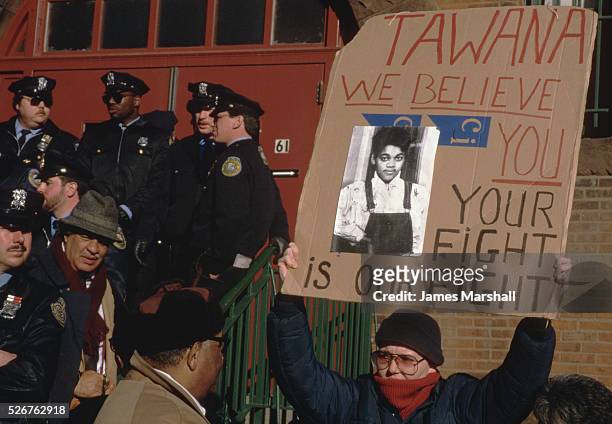 Demonstrator near a group of police officers at the Poughkeepsie Armory holds up a sign in favor of Tawana Brawley.