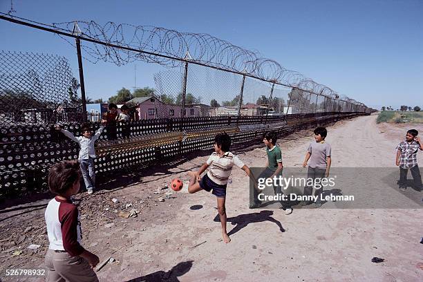 Children Playing Soccer Along Border Fence