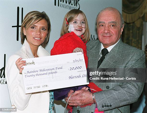 Victoria Beckham presents Kirsty Howard, a patient at the Francis House Hospice in Manchester being held by store owner Mr. Al Fayed, with a cheque...