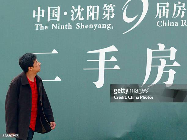 Chinese man walks past a billboard advertising secondhand real estate at a real estate fair on April 21, 2005 in Shenyang of Liaoning Province,...